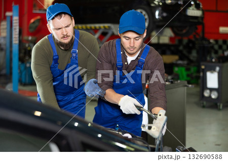 Skilled male auto mechanics in blue overalls repairing automobile Skilled male auto mechanics in blue overalls repairing automobile 132690588