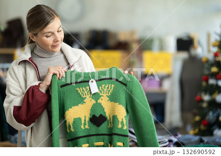 Positive young woman choosing sweater in clothing store 132690592