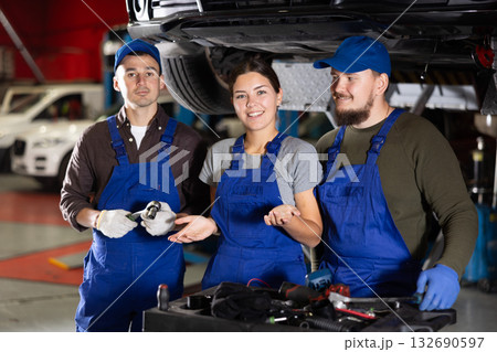 Portrait of professional auto mechanics in auto repair shop next to car on lift 132690597