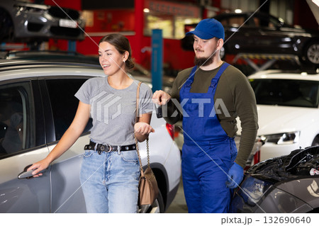 Young male mechanic giving car keys to woman client Young male mechanic giving car keys to woman client 132690640