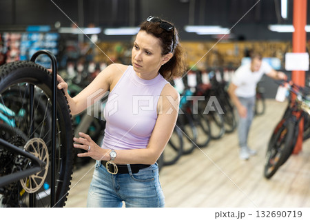 Female cyclist carefully examining bike wheel in store Female cyclist carefully examining bike wheel in store 132690719