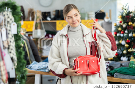 adult woman chooses fashionable handbags in a store against the background of a Christmas tree adult woman chooses fashionable handbags in a store against the background of a Christmas tree 132690737
