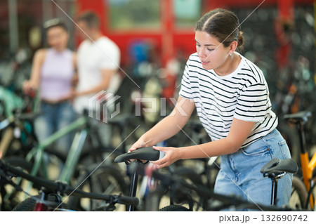 Girl assessing saddle while choosing bicycle in store 132690742