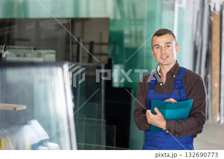 Positive factory worker with clipboard standing in glass workshop Positive factory worker with clipboard standing in glass workshop 132690773