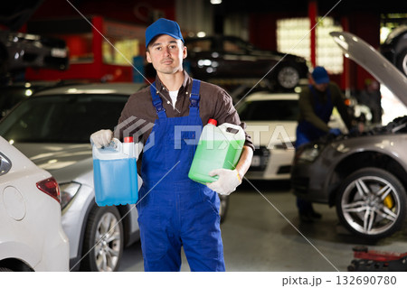 Positive male worker of car workshop holding full plastic cans Positive male worker of car workshop holding full plastic cans 132690780
