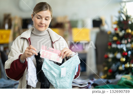 Young woman choosing panty sets on Christmas tree background in clothing store 132690789