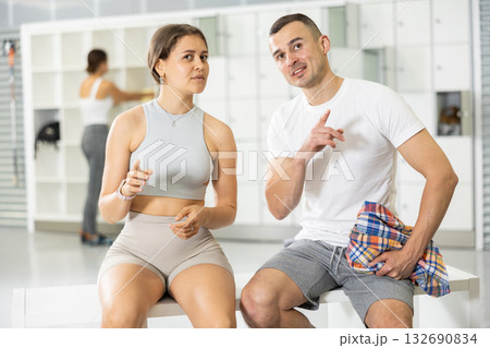 Young woman and man sitting, exchanged couple of phrases in locker room after changing clothes 132690834
