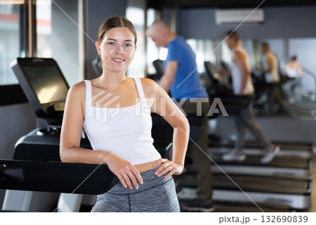 Young woman posing by treadmill in gym Young woman posing by treadmill in gym 132690839