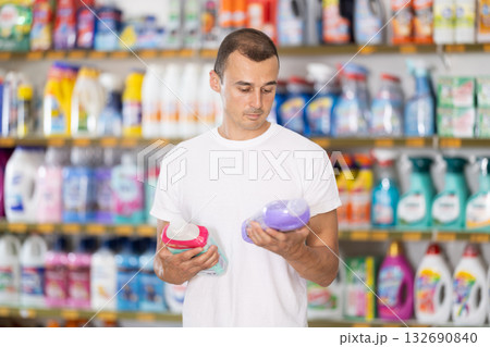 Man carefully selects cleaning product in industrial section of supermarket Man carefully selects cleaning product in industrial section of supermarket 132690840