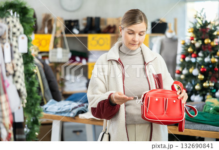 adult woman chooses fashionable handbags in a store against the background of a Christmas tree 132690841