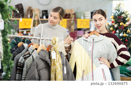 Two uncertain women choosing coat or jacket in clothing store 132690875