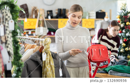 Woman client looks at products in store, choose closely ladys bag 132690936