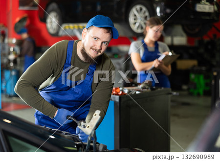 Professional mechanic man in uniform repairing car in auto repair garage Professional mechanic man in uniform repairing car in auto repair garage 132690989