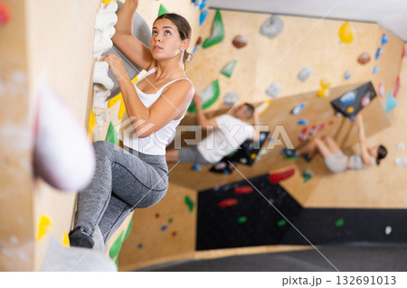 Young woman climbs steep artificial wall in sports complex and trains endurance Young woman climbs steep artificial wall in sports complex and trains endurance 132691013