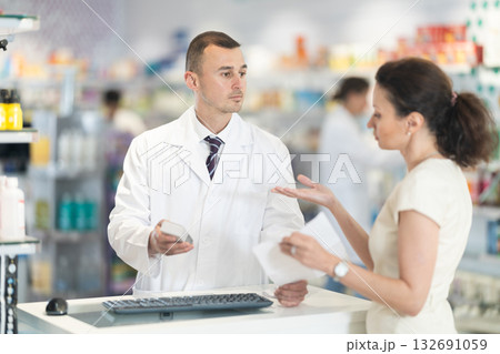 Male pharmacist consulting woman client about medicament in box according to recipe Male pharmacist consulting woman client about medicament in box according to recipe 132691059