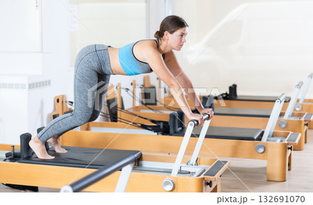 Girl practicing exercises on Pilates reformer during rehabilitation session 132691070
