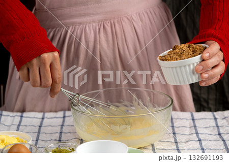 Hands preparing to mix brown sugar into a bowl of creamed butter and eggs, perfect for holiday cookie baking 132691193