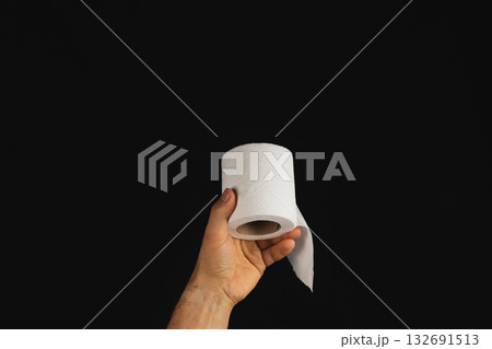 Holding a roll of toilet paper in a dark setting with a hand 132691513