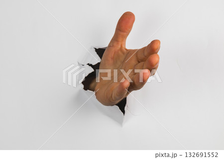 Hand reaching through a hole in a white wall creating a unique visual effect Hand reaching through a hole in a white wall creating a unique visual effect 132691552