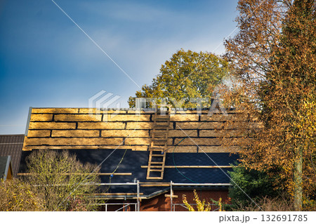 Roof Under Construction With Wooden Planks, Ladder And Autumn Trees Under Clear Blue Sky Roof Under Construction With Wooden Planks, Ladder And Autumn Trees Under Clear Blue Sky 132691785