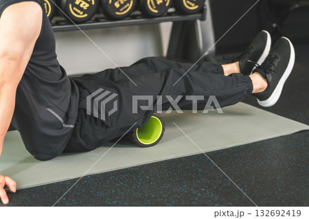 ジムでフォームローラーを使ってふくらはぎの筋膜リリースをする男性 ジムでフォームローラーを使ってふくらはぎの筋膜リリースをする男性 132692419