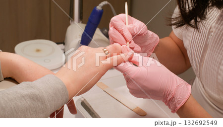 Gel nails. Professional manicure procedure. Manicurist female hands making hardware machine to beauty salon client using wooden stick to push back cuticle. 132692549