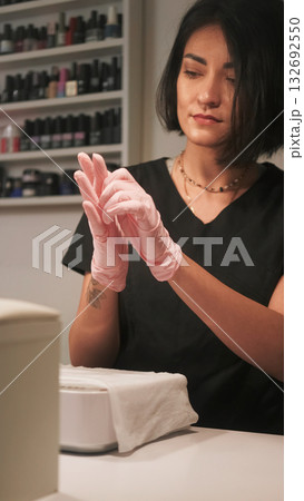 Beautician work. Nail treatment. Woman wearing pink latex medical sterilized protective gloves hands getting ready for manicure procedure. 132692550