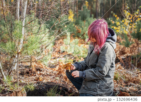 Girl with pink hair foraging mushrooms in autumn forest 132696436