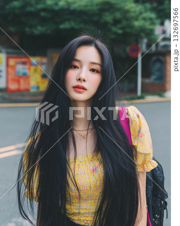 Girl with long black hair wearing a yellow top stands on a city street in Korea during daytime 132697566