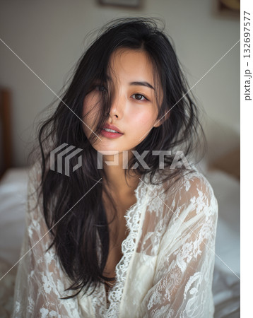 Woman with long dark hair wearing lace top in a cozy bedroom during midday light 132697577