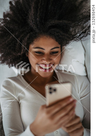 Portrait of young woman using smartphone, lying in bed. Portrait of young woman using smartphone, lying in bed. 132698454