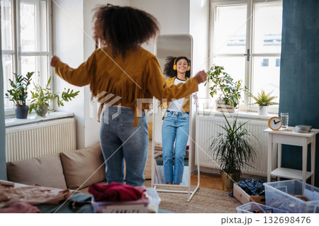 Young woman dancing in front of mirror with headphones. Young woman dancing in front of mirror with headphones. 132698476