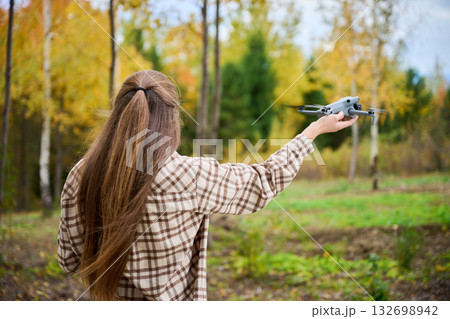 A young person stands in a vibrant forest during autumn, ready to launch a drone into the colorful trees and nature. The scene is peaceful and full of life. 132698942