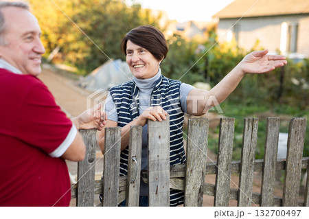 Two gardeners friendly talking outdoors next to wooden fence of country estate on day 132700497