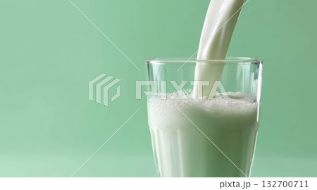 Creamy liquid stream, close up of white milk being poured into a transparent glass, creating a foamy texture. Fresh dairy drink on a pastel background. 132700711