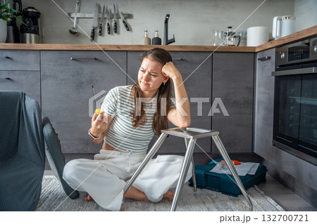 Frustrated young woman trying to assemble a chair with tools on the floor. Concept of difficulty and struggle in do it yourself project. 132700721