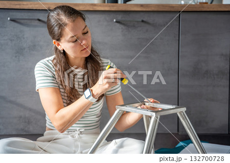 Young woman sitting on the floor assembling a chair with tools. Concept of female independence and do it yourself lifestyle. 132700728