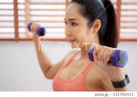 Young asian woman in sportswear workout with dumbbells for strength in living room at home. Young asian woman in sportswear workout with dumbbells for strength in living room at home. 132702415