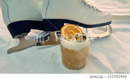 Cocktail with toasted marshmallow and dried orange near white ice skates Cocktail with toasted marshmallow and dried orange near white ice skates 132702448