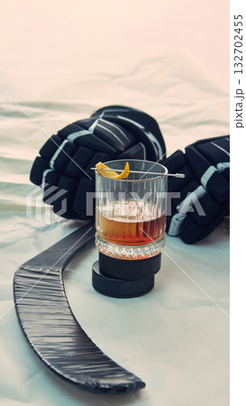 Whiskey glass with orange zest near hockey gloves and stick on white surface Whiskey glass with orange zest near hockey gloves and stick on white surface 132702455