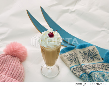 Coffee with whipped cream and cherry beside pink hat blue mittens and skis Coffee with whipped cream and cherry beside pink hat blue mittens and skis 132702460
