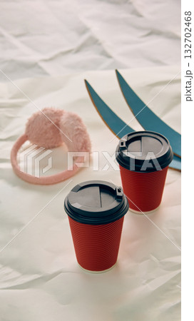 Two red coffee cups with pink earmuffs and blue skis on white background 132702468