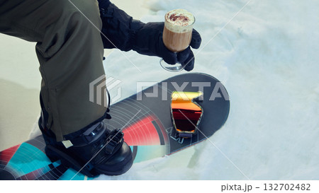 Snowboarder in winter outfit holding hot drink on snow slope 132702482