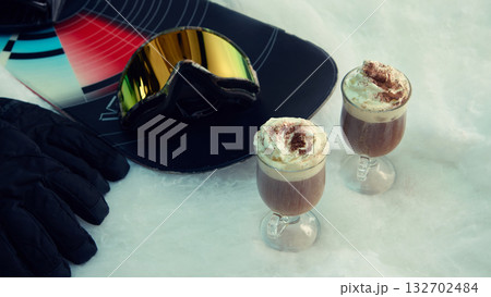 Two hot drinks with whipped cream and snowboard gear on snow surface Two hot drinks with whipped cream and snowboard gear on snow surface 132702484