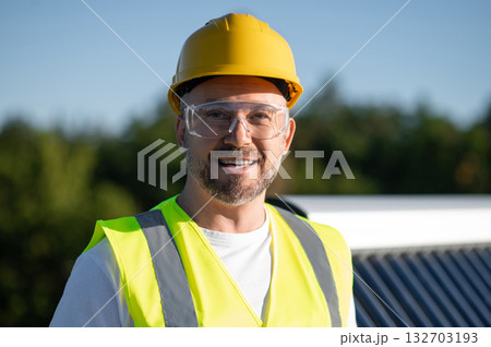 Technician standing confidently on rooftop posing near solar panels 132703193