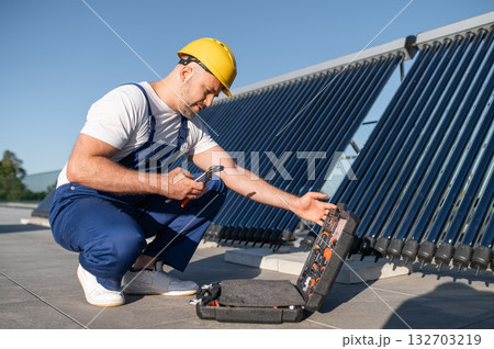 Male installer in overalls checking solar heating system outdoors Male installer in overalls checking solar heating system outdoors 132703219