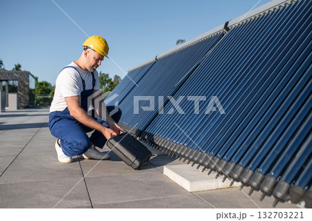 Man in helmet and uniform inspecting solar collectors on building Man in helmet and uniform inspecting solar collectors on building 132703221
