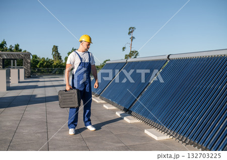 Technician in blue overalls inspecting solar panels on rooftop Technician in blue overalls inspecting solar panels on rooftop 132703225