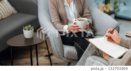 Counselor documents notes in a calm consultation setting while client holds a coffee cup 132703869