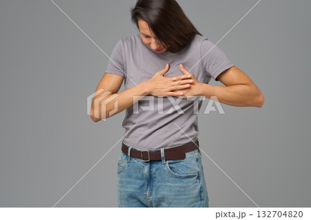 Woman holding chest with both hands, bending forward in pain, neutral background Woman holding chest with both hands, bending forward in pain, neutral background 132704820